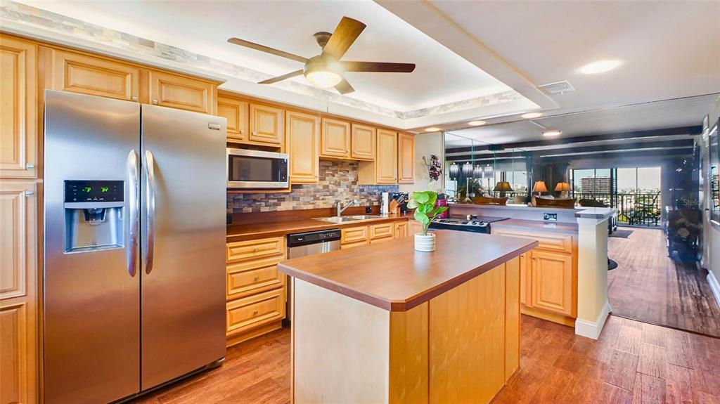 A kitchen with wood cabinets, stainless steel appliances, a center island, and a tile backsplash — 7150 SUNSET UNIT 903E, ST PETE BEACH, FL