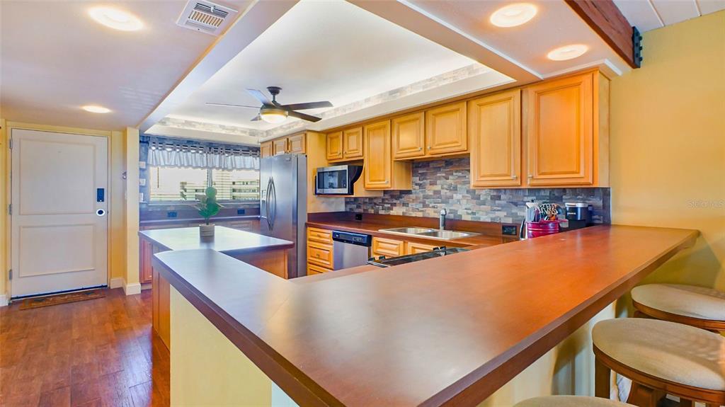 A kitchen features wood cabinets, a stone backsplash, a breakfast bar, and stainless steel appliances — 7150 SUNSET UNIT 903E, ST PETE BEACH, FL