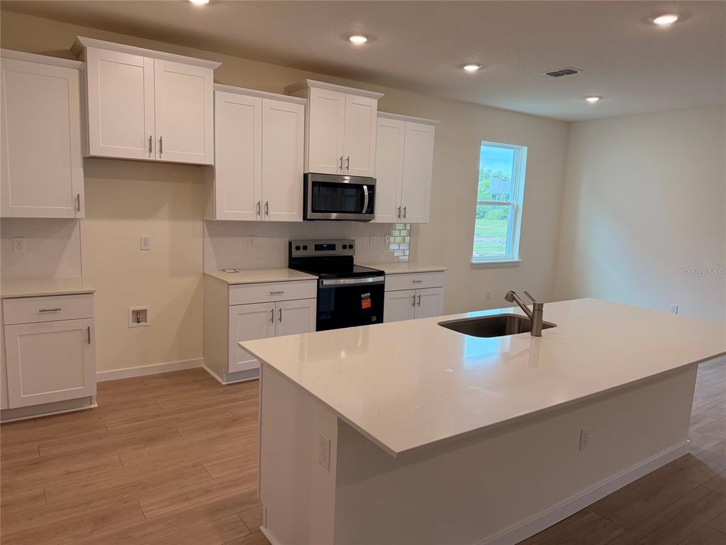 A modern kitchen features a large quartz island, white cabinetry, and stainless steel appliances — 3042 KINGSMAN TRAIL, ORMOND BEACH, FL