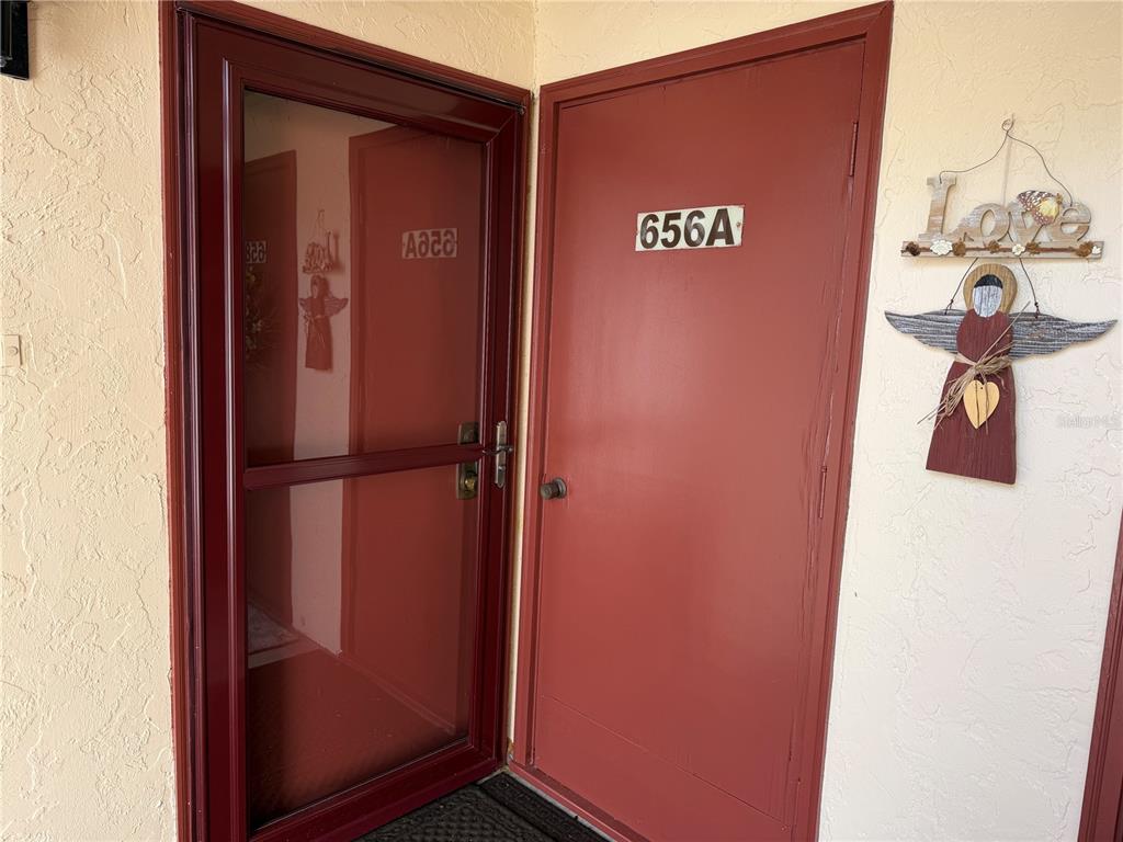 A red front door with a storm door and a decorative angel wall hanging — 656 MIDWAY DRIVE UNIT A, OCALA, FL