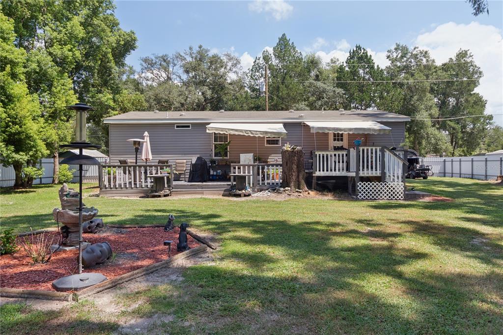 A single-story house with gray siding features a large wooden deck and two retractable awnings — 16711 PETRAS LANE, SPRING HILL, FL