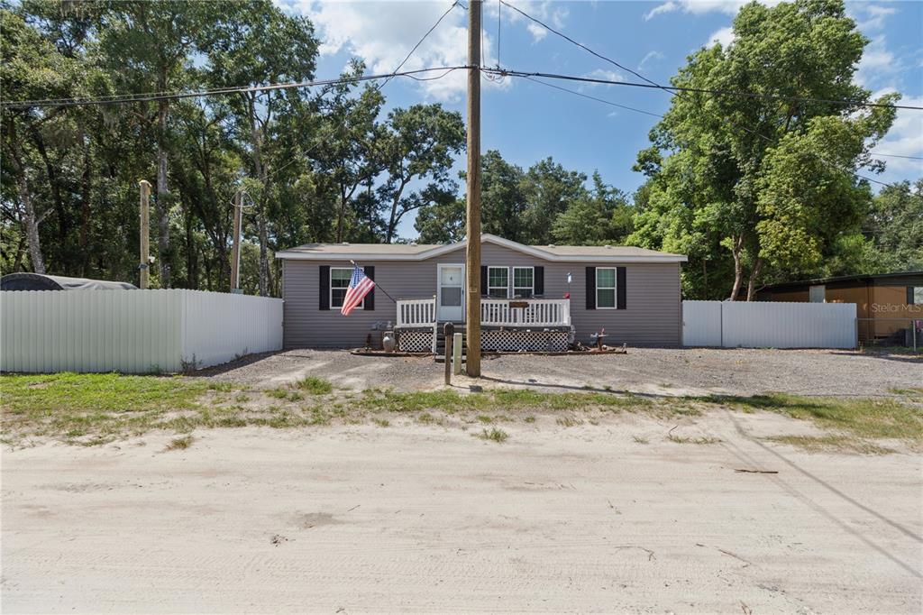 A single-story manufactured home with a white fence and a gravel driveway — 16711 PETRAS LANE, SPRING HILL, FL