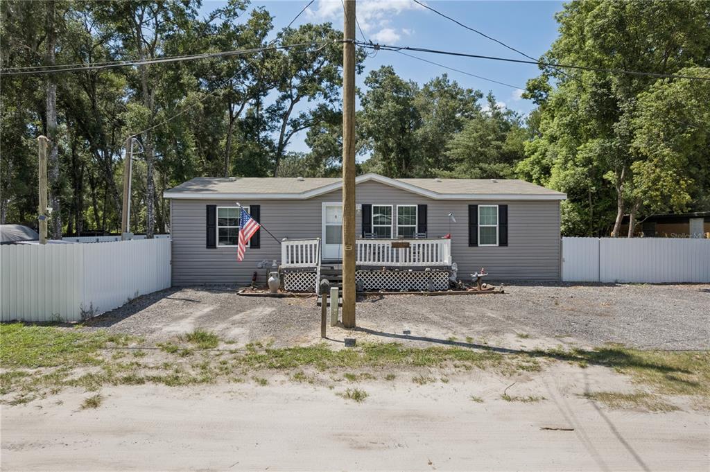 A single-story manufactured home with grey siding, a front porch, and a gravel driveway — 16711 PETRAS LANE, SPRING HILL, FL