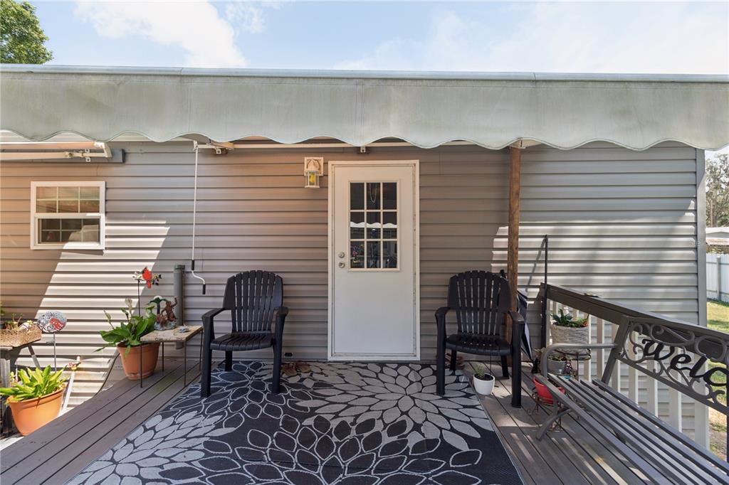 A gray-sided home exterior features a white door, a deck, and two black chairs — 16711 PETRAS LANE, SPRING HILL, FL