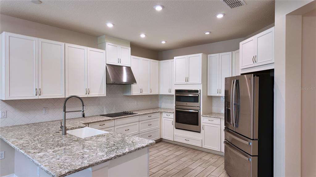 A kitchen features white cabinetry, granite countertops, stainless steel appliances, and light wood-look tile flooring — 1287 VERDANT GLADE PLACE, WINTER PARK, FL