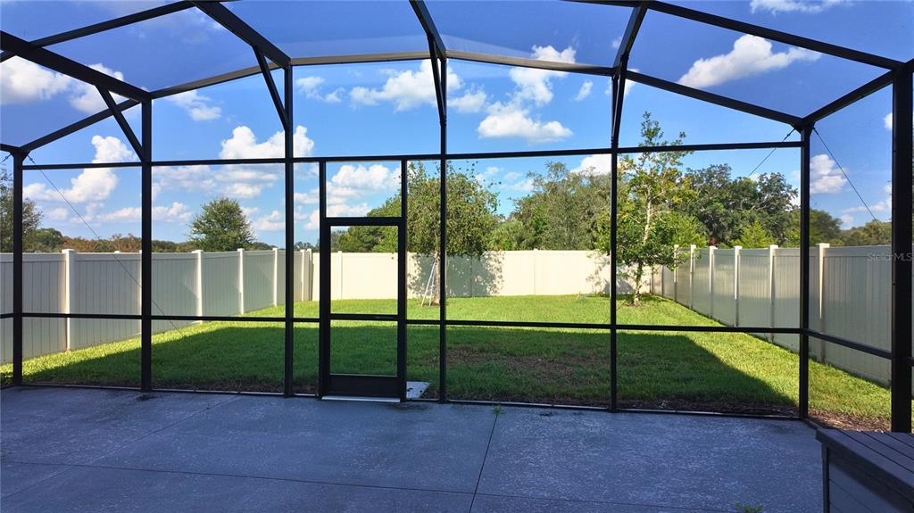 A screened-in concrete patio overlooks a grassy backyard enclosed by a white vinyl fence — 1287 VERDANT GLADE PLACE, WINTER PARK, FL
