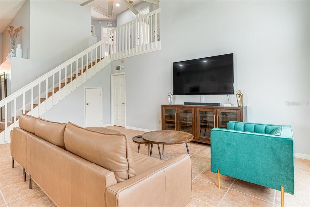 A living room features a tan leather sofa, a teal armchair, and a wooden staircase — 418 RIGGS CIRCLE, DAVENPORT, FL