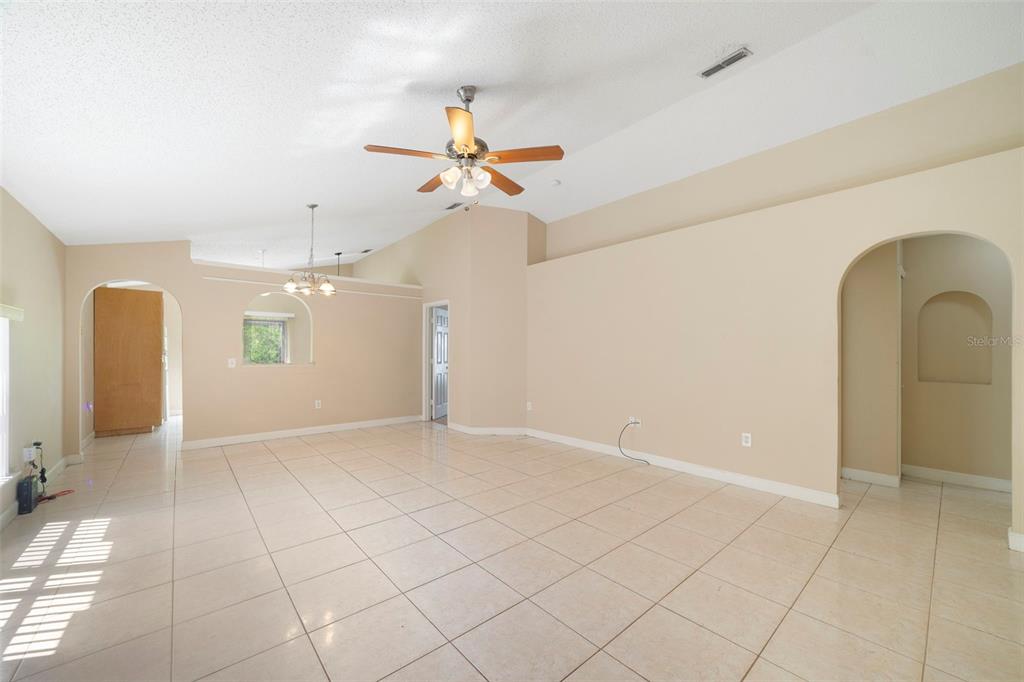 An open-concept living area features vaulted ceilings, beige tile flooring, and arched doorways — 13142 ODYSSEY LAKE WAY, ORLANDO, FL