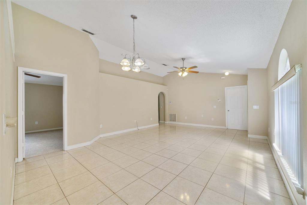 An empty room with beige walls, tile flooring, a vaulted ceiling, and a chandelier — 13142 ODYSSEY LAKE WAY, ORLANDO, FL