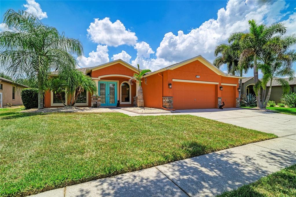 A single-story orange house with a three-car garage and palm trees in the front yard — 316 STAR SHELL DRIVE, APOLLO BEACH, FL