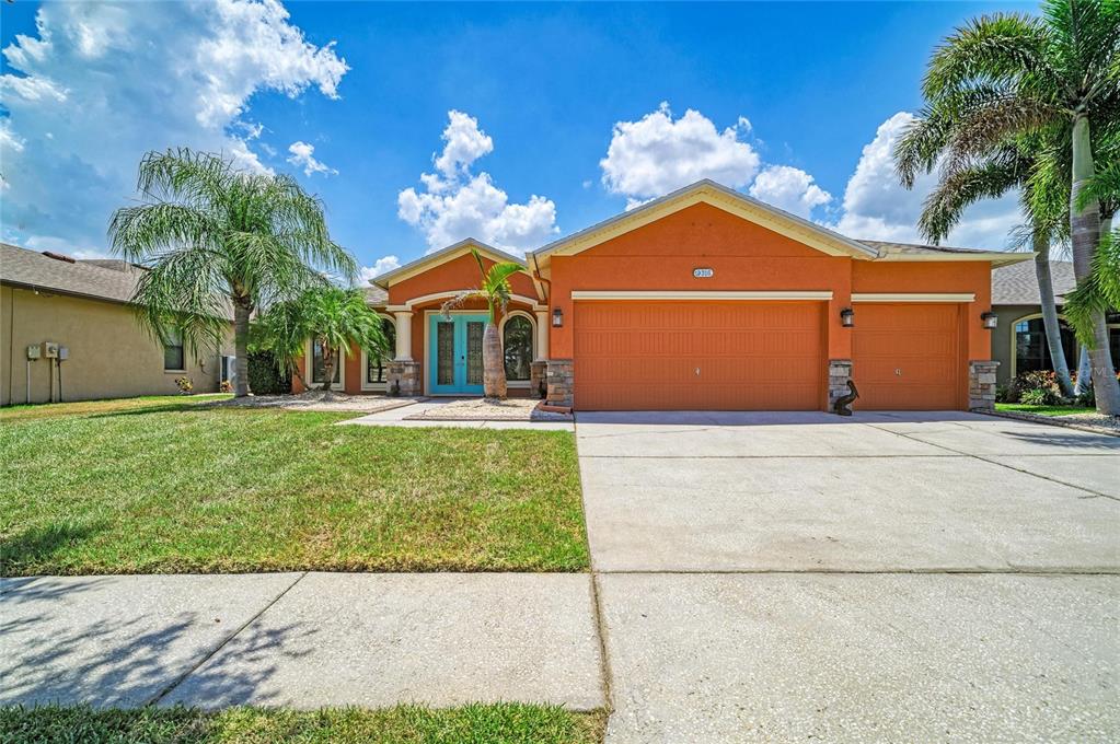 A single-story orange house with a three-car garage and a bright blue front door — 316 STAR SHELL DRIVE, APOLLO BEACH, FL