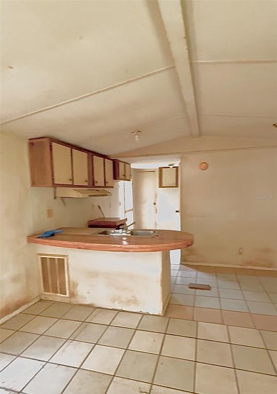A kitchen with a breakfast bar, light-colored tile flooring, and wood-toned cabinets — 19399 FORT DADE AVENUE, BROOKSVILLE, FL