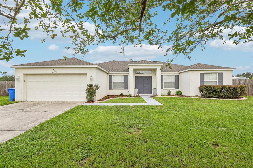 A single-story house with a beige stucco exterior, a two-car garage, and a front lawn — 2206 WOODEN SHOE WAY, PLANT CITY, FL
