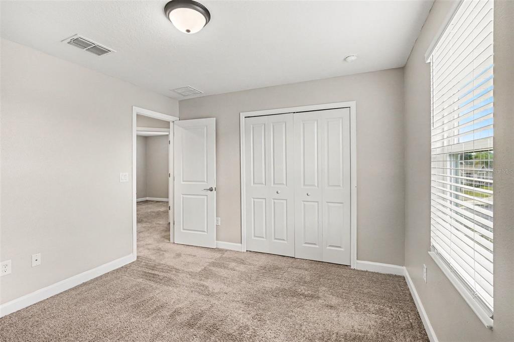 An empty bedroom features beige walls, gray carpet, and a window with white blinds — 490 BRUNSWICK DRIVE, DAVENPORT, FL