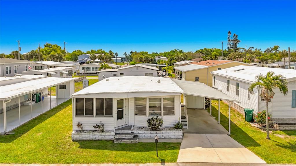 A white mobile home with a carport and a screened front porch sits on grass — 80 DEL RIO DRIVE, PALMETTO, FL