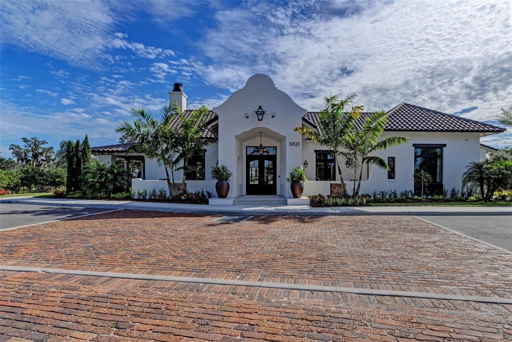 A white stucco house with a tiled roof and brick driveway stands under a blue sky — 11815 RIVER SHORES TRAIL, PARRISH, FL