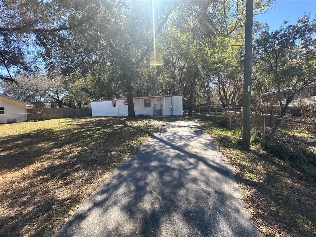 A white mobile home sits at the end of a paved driveway under large trees — 9150 SE 142ND PLACE, SUMMERFIELD, FL