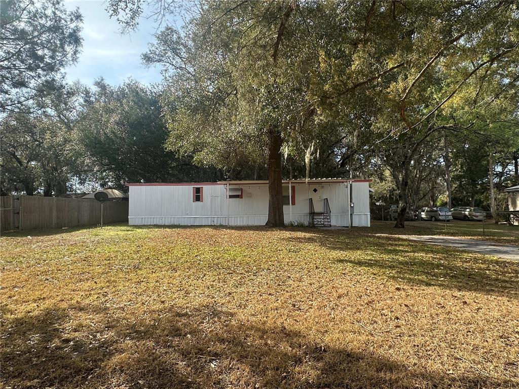 A single-story mobile home sits on a grassy lot shaded by large trees — 9150 SE 142ND PLACE, SUMMERFIELD, FL