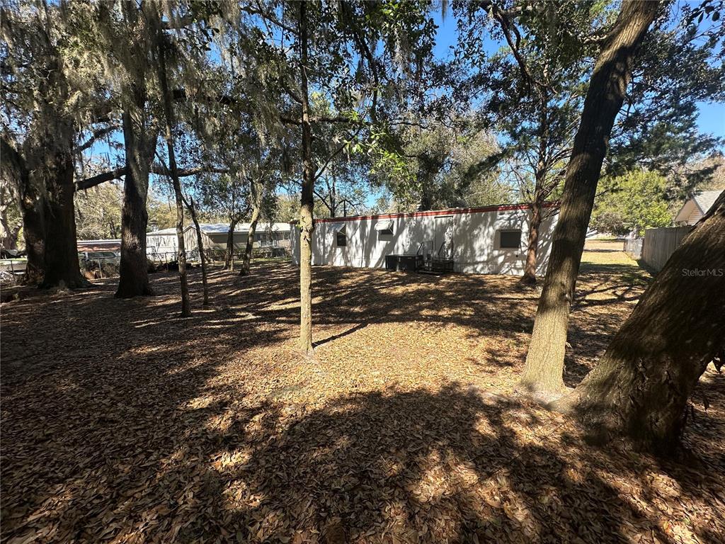A mobile home sits on a wooded lot covered in fallen leaves under large trees — 9150 SE 142ND PLACE, SUMMERFIELD, FL