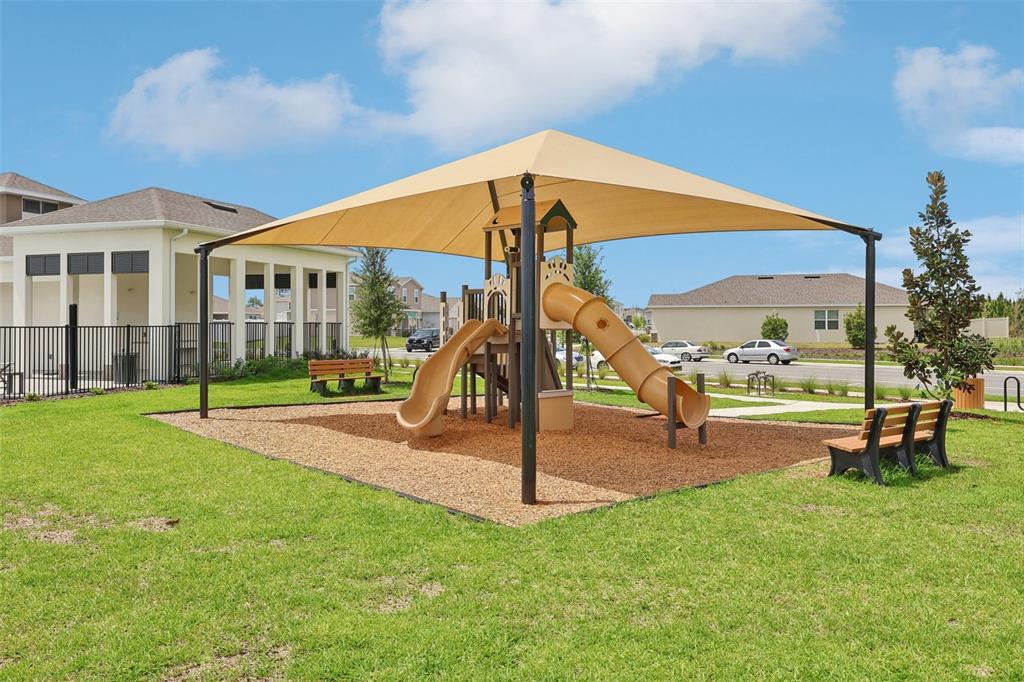 A playground with a tan shade canopy and two slides sits on a wood-chipped area — 1819 LATTICE WAY, ST CLOUD, FL