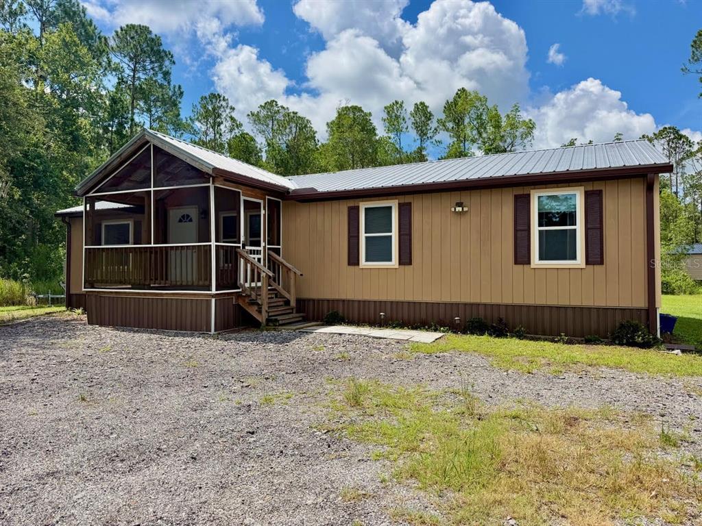 A house with a front porch sits on a large, grassy lot surrounded by trees — 5171 MAHOGANY BOULEVARD, BUNNELL, FL