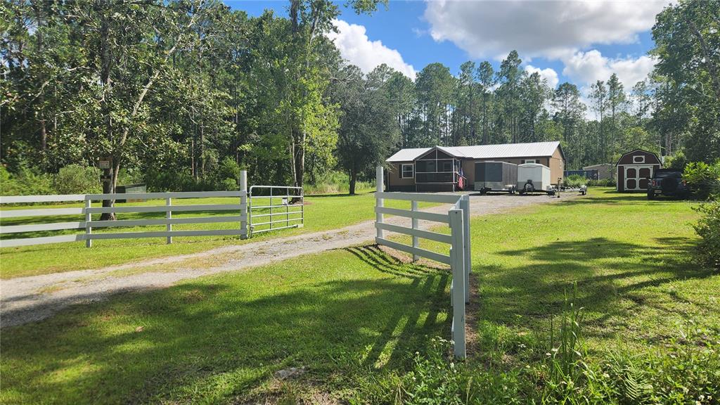 A single-story house with brown siding and a metal roof sits on a gravel lot — 5171 MAHOGANY BOULEVARD, BUNNELL, FL