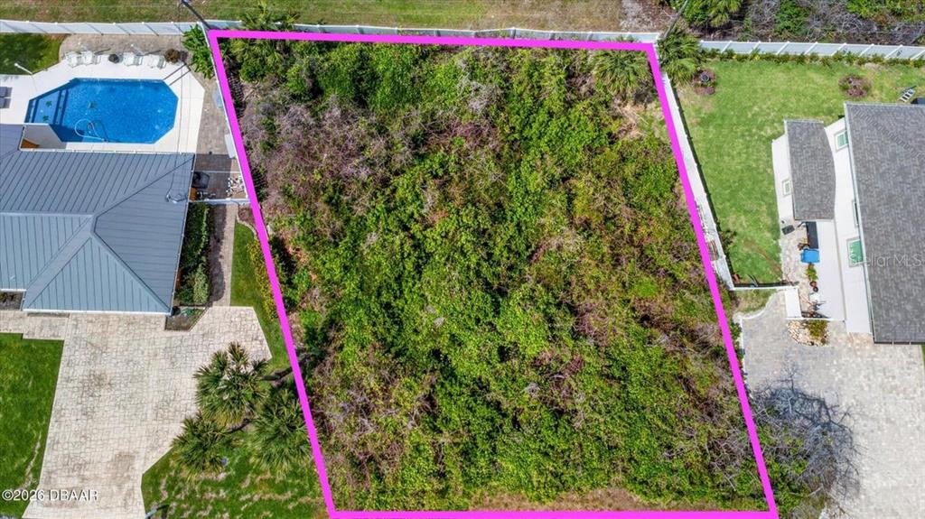 An aerial view shows a vacant, overgrown lot outlined in pink between two residential properties — 28 OCEAN BREEZE CIRCLE, ORMOND BEACH, FL