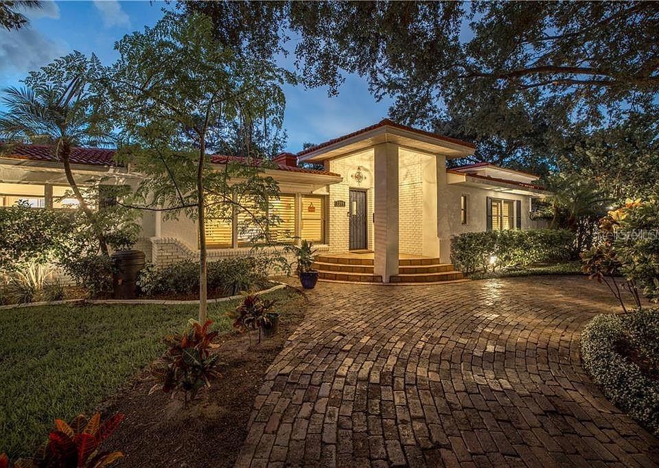 A single-story house with a brick driveway, white brick facade, and a tiled roof at dusk — 2200 2ND STREET N, ST PETERSBURG, FL