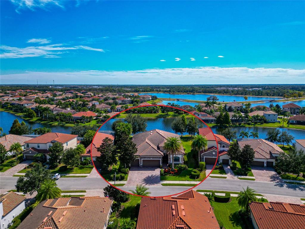 An aerial view shows a single-family home with a tiled roof situated near a lake — 13026 RAMBLEWOOD TRAIL, BRADENTON, FL