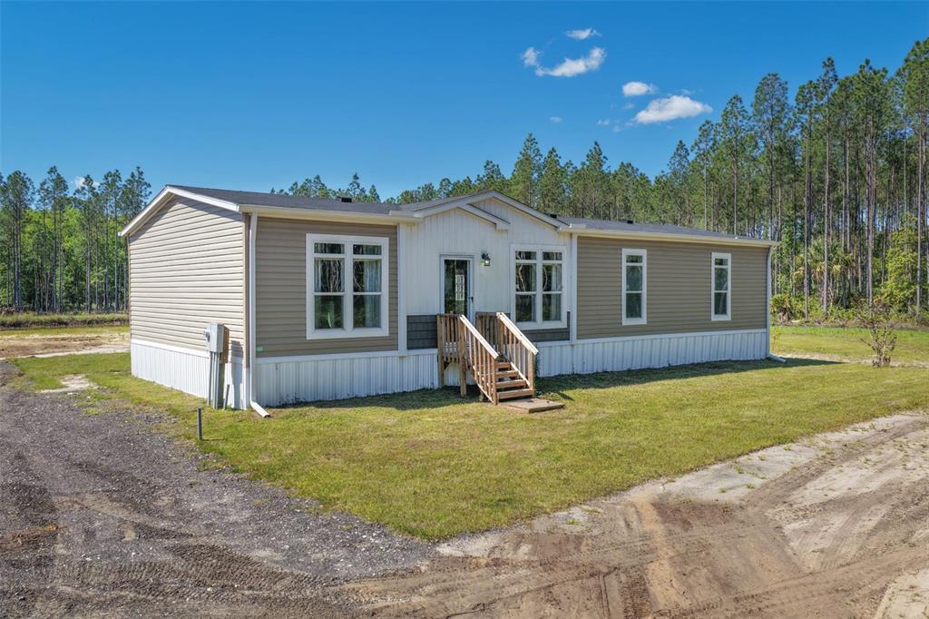 A single-story manufactured home with tan and white siding sits on a grassy lot — 15539 COUNTY RD 305, BUNNELL, FL