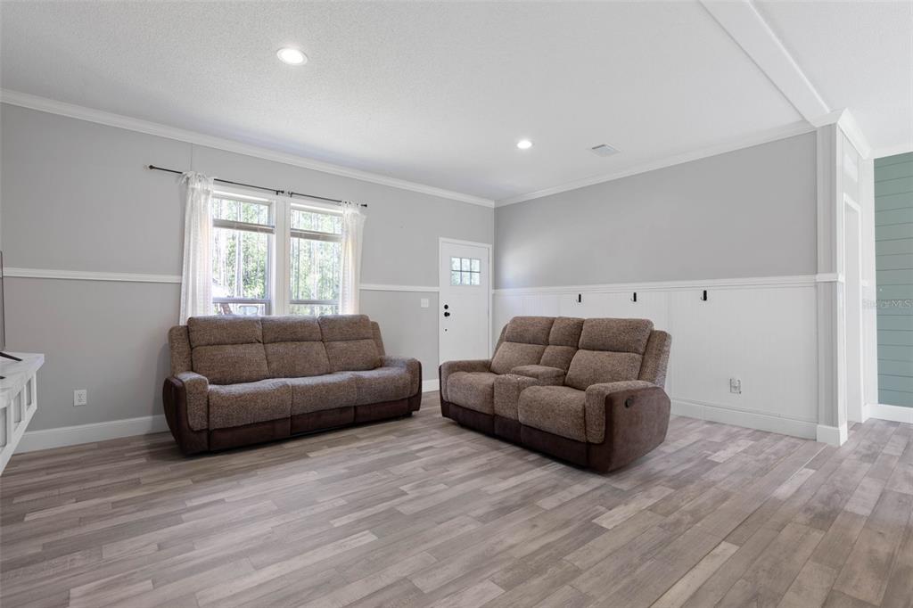 A living room features light gray walls, white wainscoting, wood-look flooring, and two brown sofas — 15539 COUNTY RD 305, BUNNELL, FL