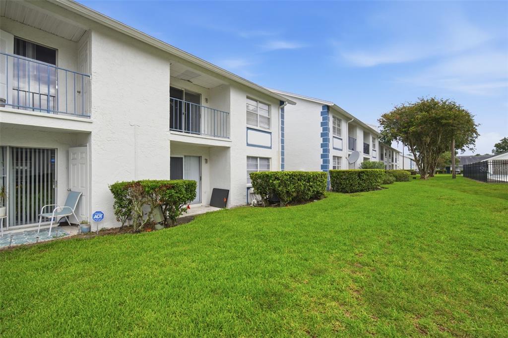 The exterior of a two-story apartment building features white stucco walls, balconies, and green lawns — 5005 BORDEAUX VILLAGE PLACE UNIT 202, TAMPA, FL
