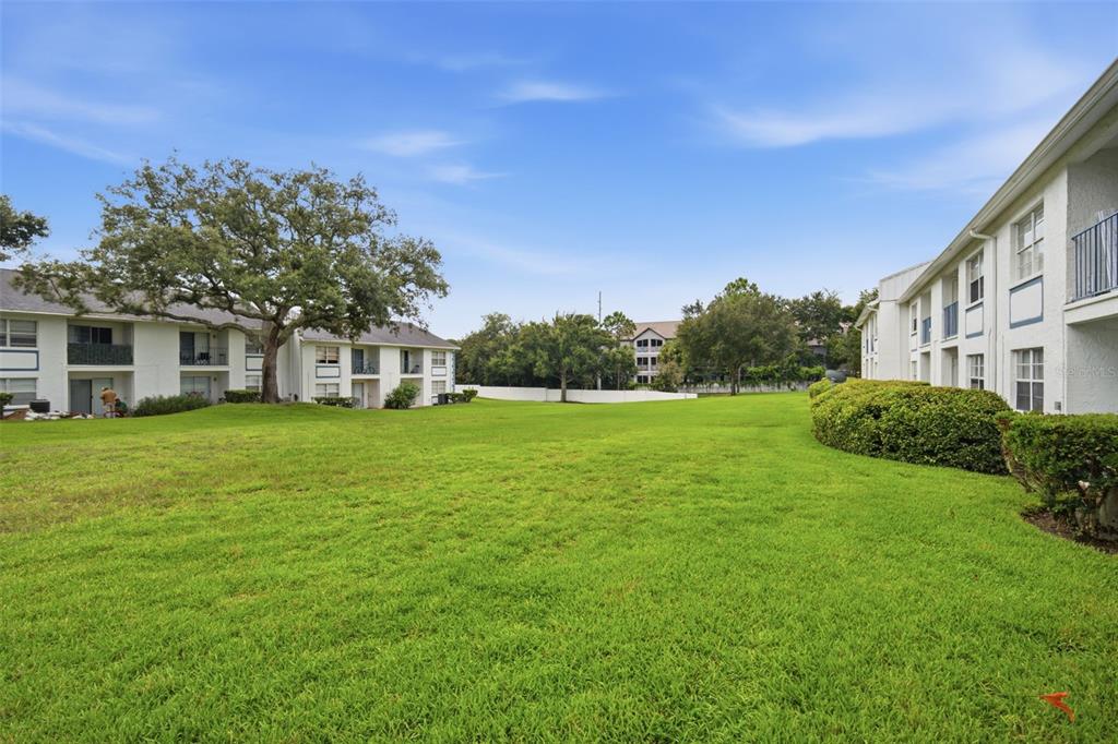 A grassy courtyard sits between two multi-story apartment buildings under a blue sky — 5005 BORDEAUX VILLAGE PLACE UNIT 202, TAMPA, FL