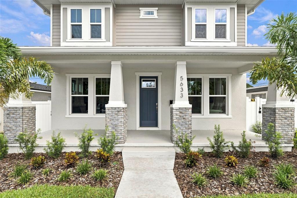 The exterior of a two-story house features a covered porch with stone-based columns and landscaping — 5633 DARTMOUTH AVENUE N, ST PETERSBURG, FL