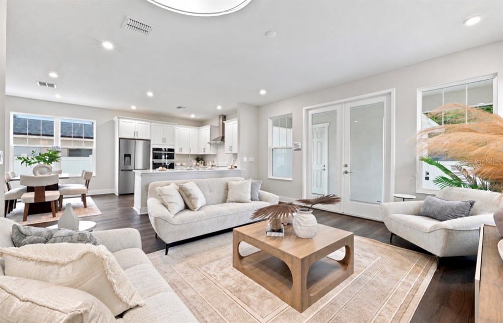 An open-concept living room and kitchen feature light-colored furniture, hardwood floors, and glass doors — 5633 DARTMOUTH AVENUE N, ST PETERSBURG, FL