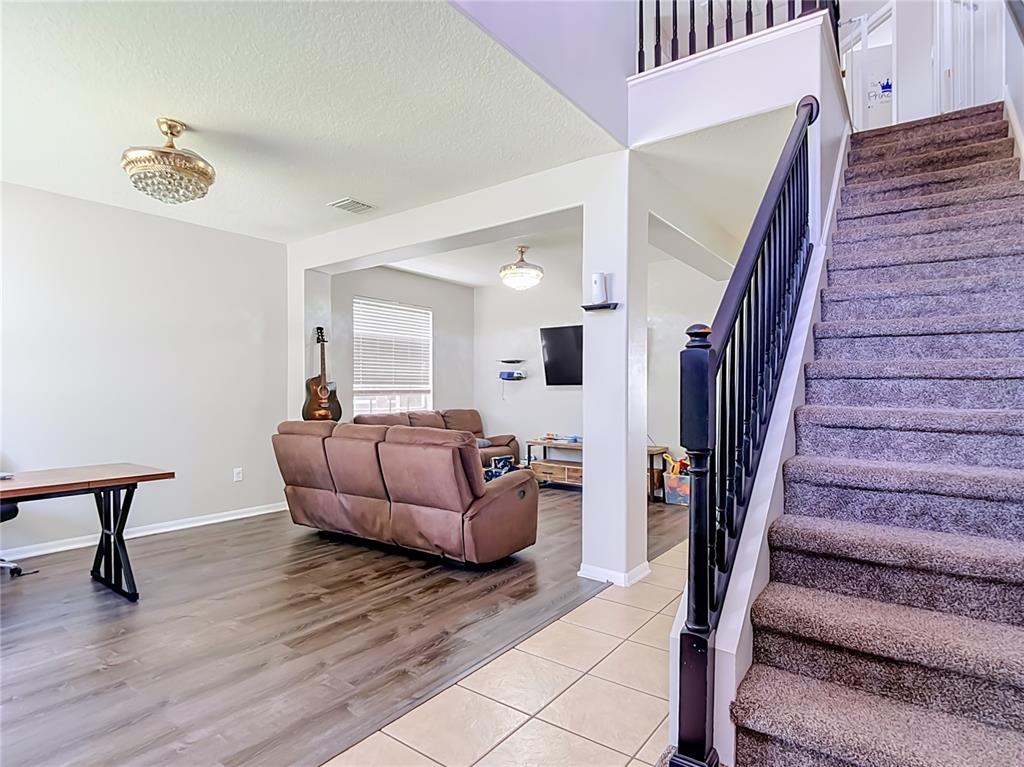 A living room with wood-look flooring, a brown sofa, and a staircase with carpeted steps — 4129 TARKINGTON DRIVE, LAND O LAKES, FL