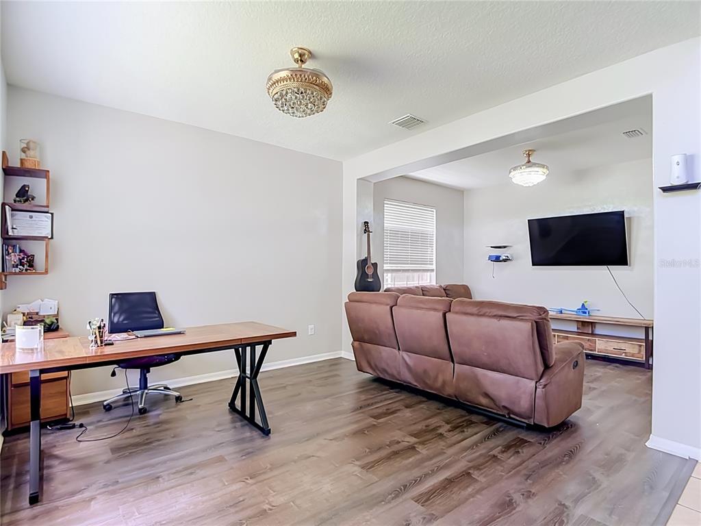 A living room and office area with wood-look flooring, a brown sofa, and a desk — 4129 TARKINGTON DRIVE, LAND O LAKES, FL