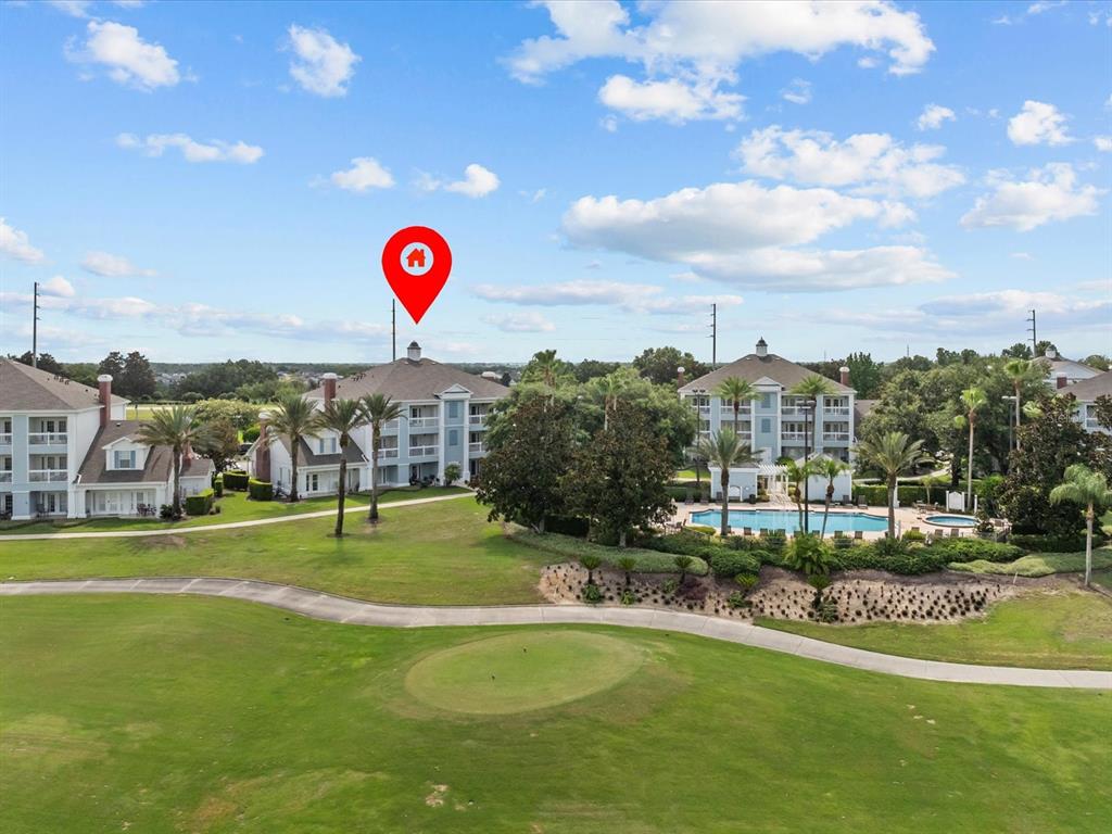 An aerial view shows multi-story apartment buildings overlooking a golf course and a swimming pool — 7615 HERITAGE CROSSING WAY UNIT 201, REUNION, FL