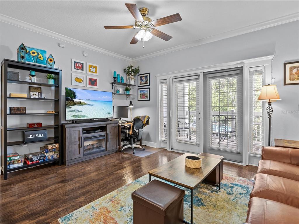 A living room features wood-look flooring, a ceiling fan, a television console, and sliding glass doors — 7615 HERITAGE CROSSING WAY UNIT 201, REUNION, FL
