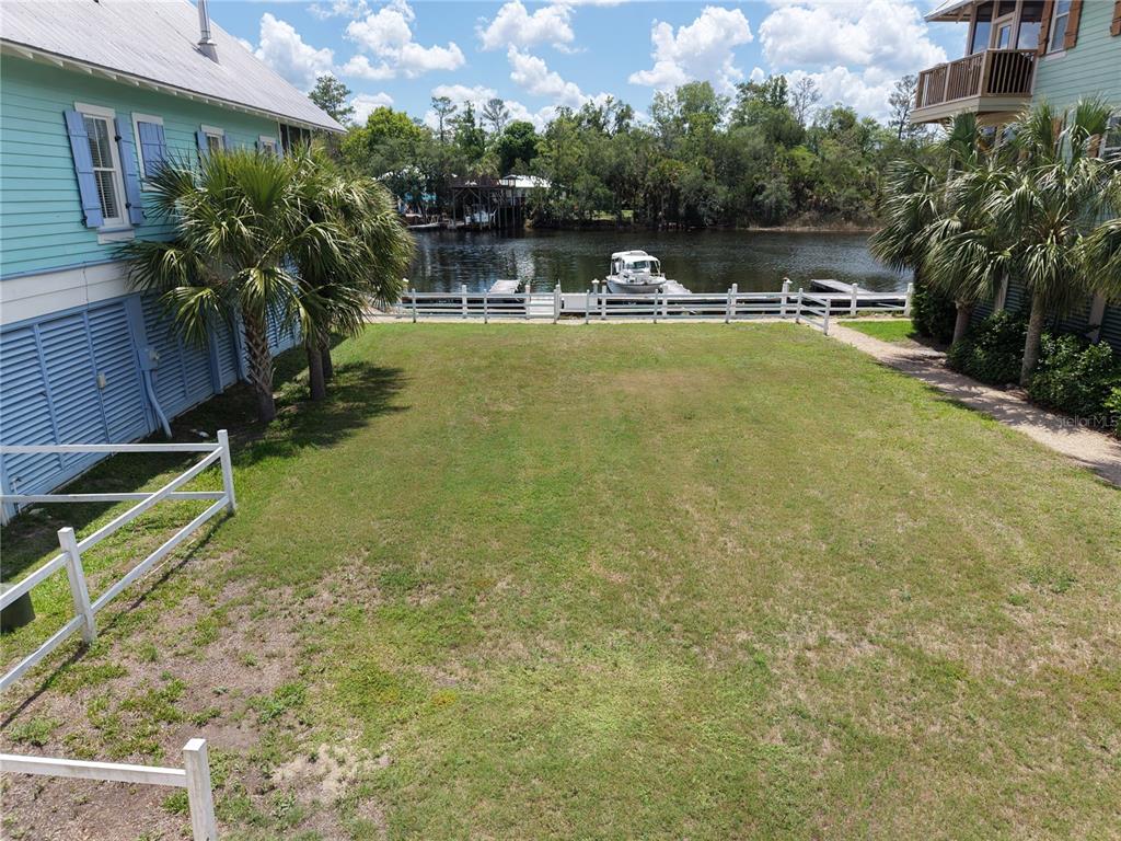 A grassy backyard sits between two houses, leading to a white fence and a boat dock — 140 RYLAND CIRCLE, STEINHATCHEE, FL