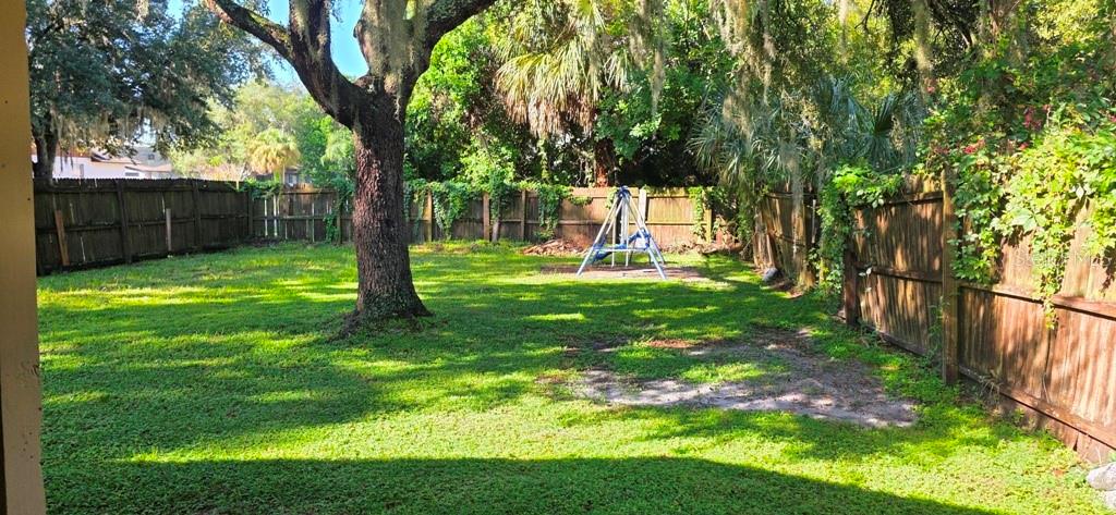 A grassy backyard features a large tree, a wooden fence, and a small swing set — 3302 ROYAL STREET, WINTER PARK, FL