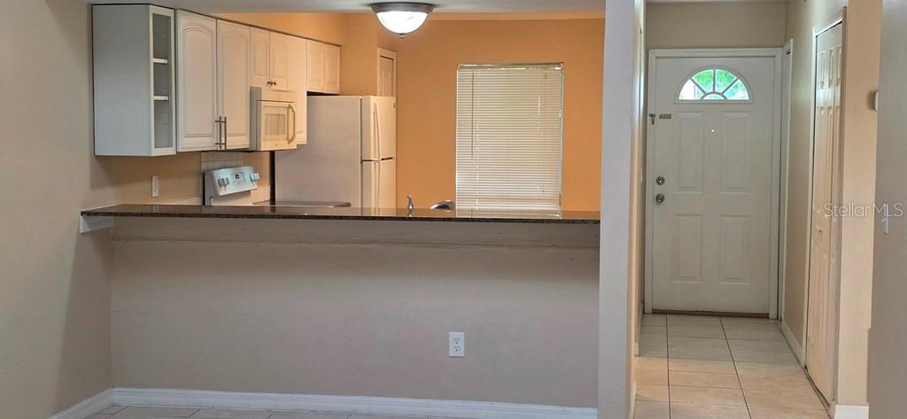 A kitchen with white cabinets and a breakfast bar overlooks a tiled entryway with a door — 3302 ROYAL STREET, WINTER PARK, FL
