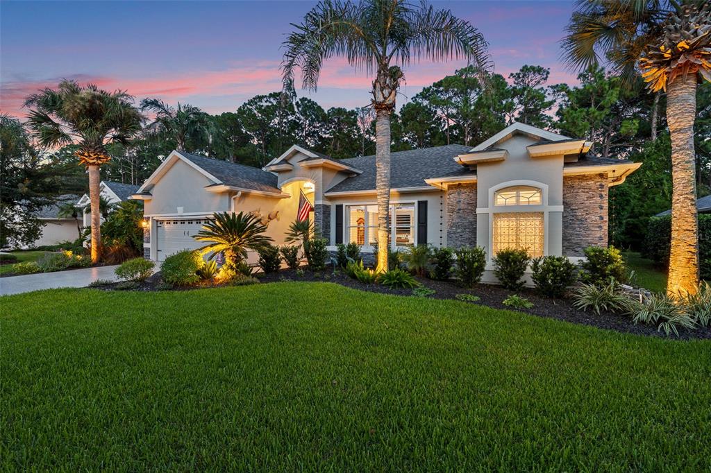 A single-story house with stone accents, a garage, and palm trees at dusk — 109 BAY LAKE DRIVE, ORMOND BEACH, FL