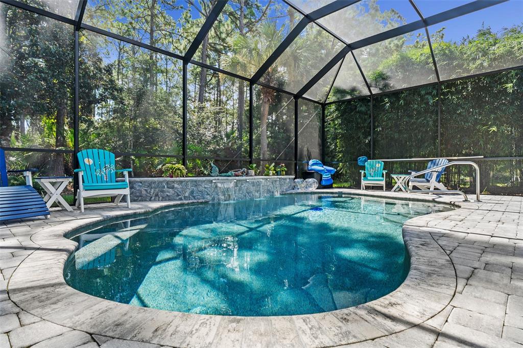 A screened-in swimming pool with a stone water feature and patio furniture in a backyard — 109 BAY LAKE DRIVE, ORMOND BEACH, FL