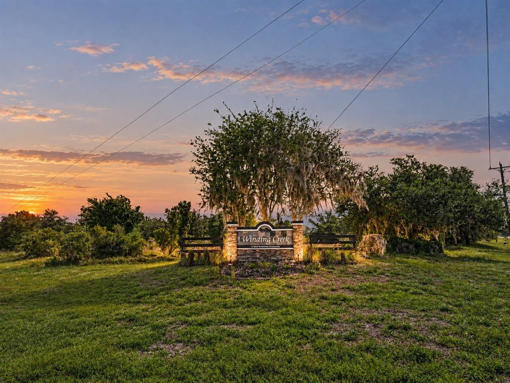A stone entrance sign for Winding Creek stands in a grassy field beneath large trees — SR-64 E, MYAKKA CITY, FL
