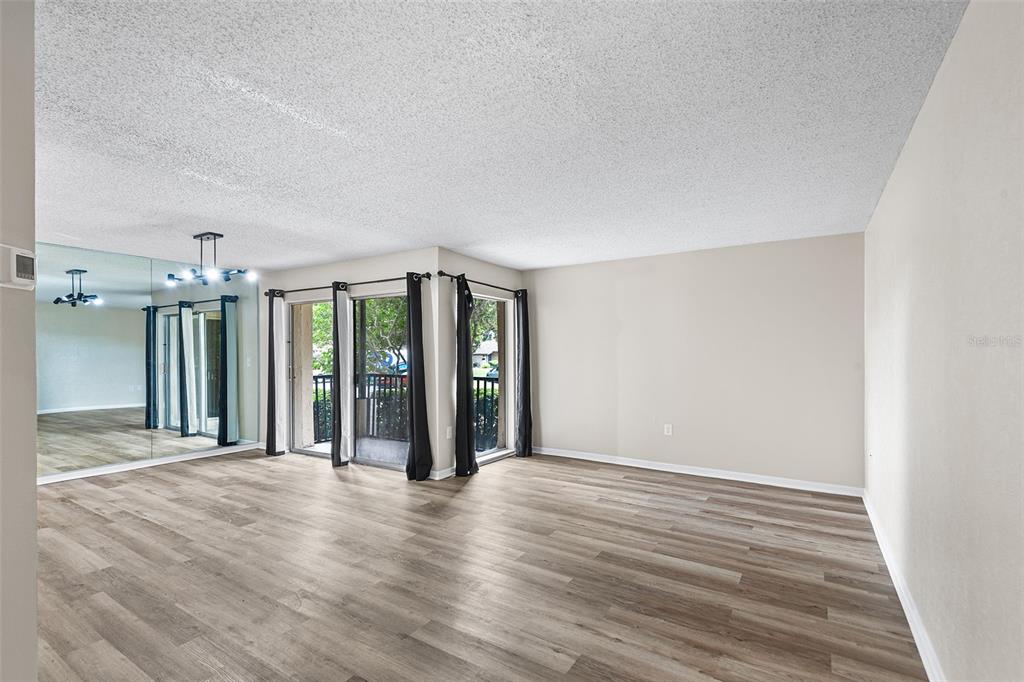 An empty living room features wood-look flooring, a mirrored wall, and sliding glass patio doors — 2025 SYLVESTER ROAD UNIT N101, LAKELAND, FL