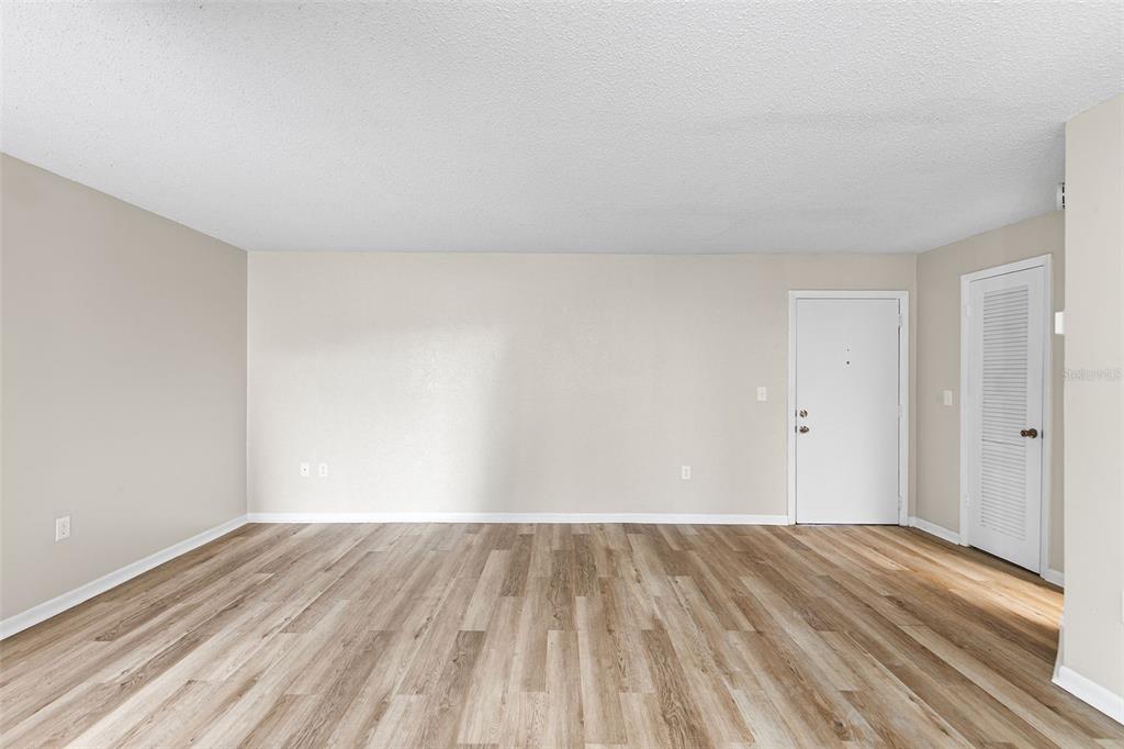 An empty room features light-colored walls, wood-look flooring, a white entry door, and a closet — 2025 SYLVESTER ROAD UNIT N101, LAKELAND, FL