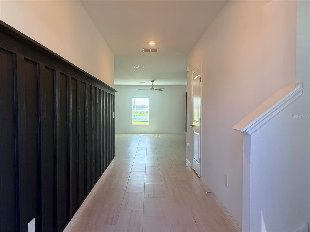 A hallway with dark wood wall paneling leads to an open living area with tile flooring — 12490 SWEET ANGEL AURA WAY, PARRISH, FL