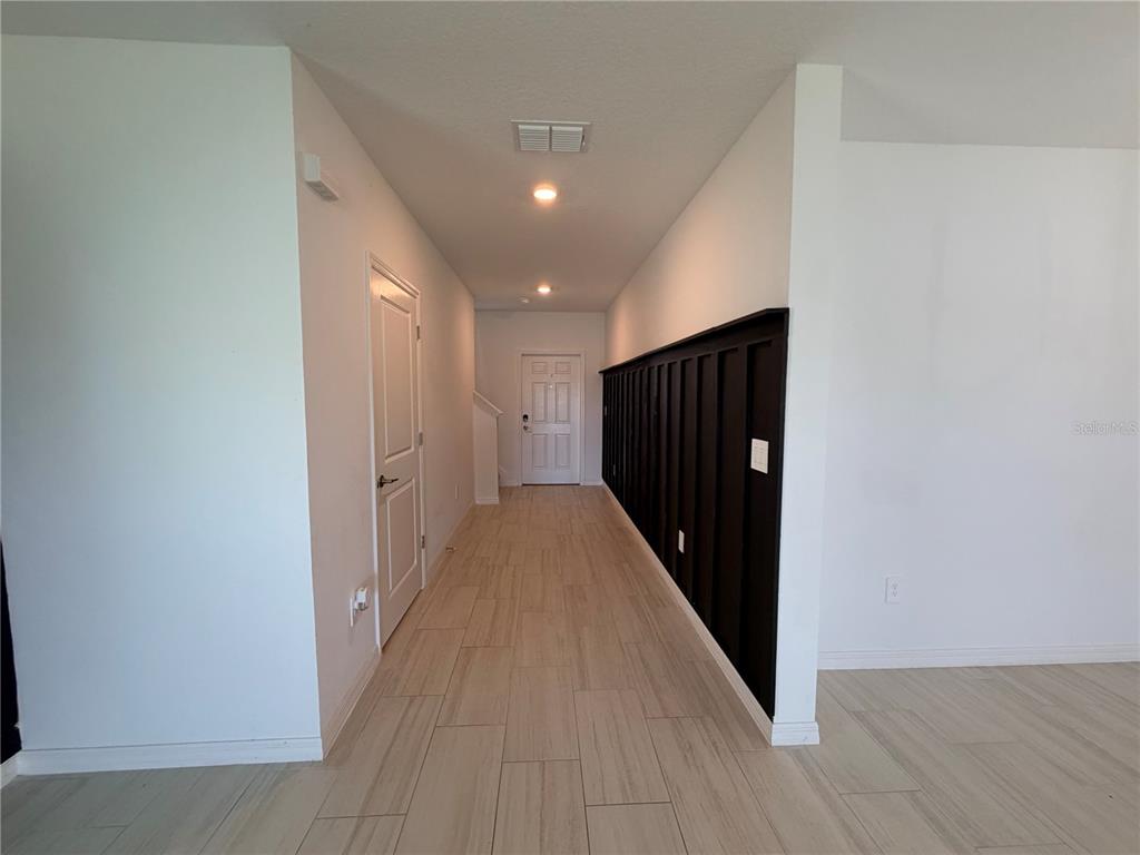 A hallway with light wood-look tile flooring features a white door and a black accent wall — 12490 SWEET ANGEL AURA WAY, PARRISH, FL