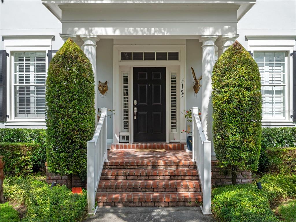 A front entrance features a black door, brick steps, and two tall, cone-shaped topiaries — 5165 FENWOOD LANE, ORLANDO, FL
